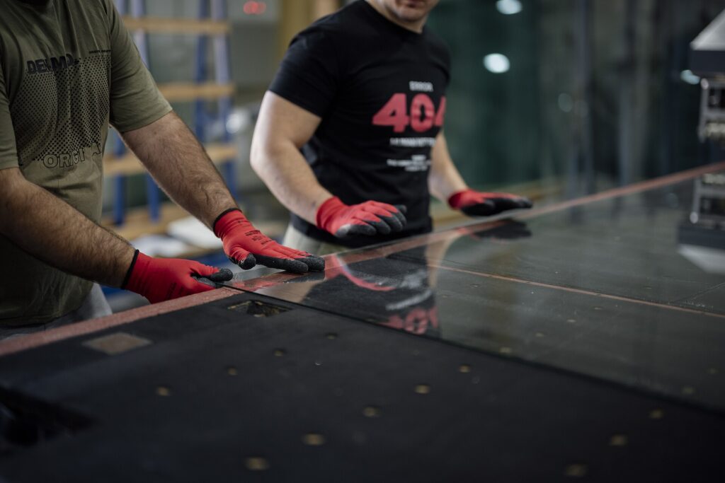 Two workers wearing cut-resistant gloves handling a large sheet of glass