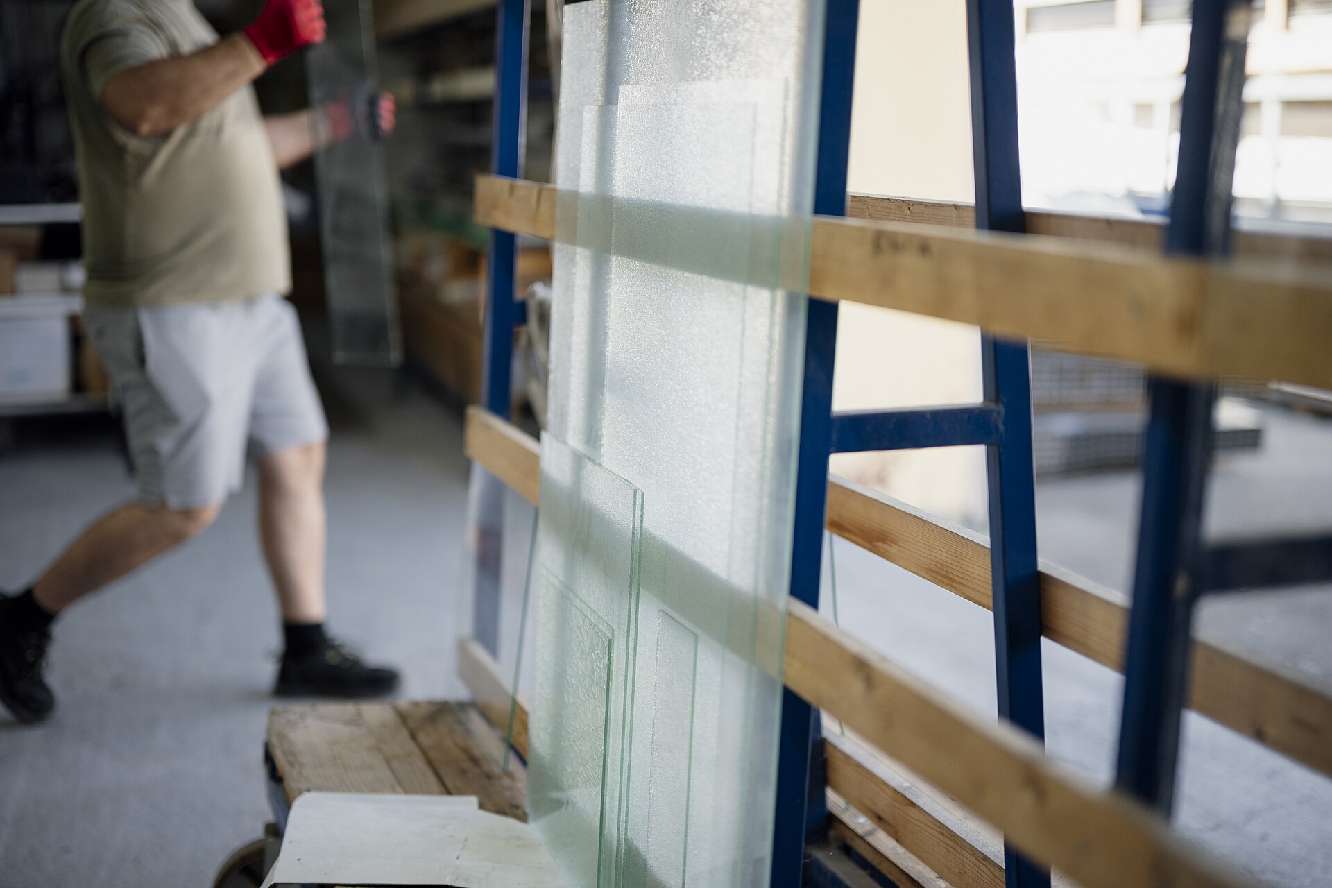 Worker moving large glass sheets stored on edge on a warehouse rack